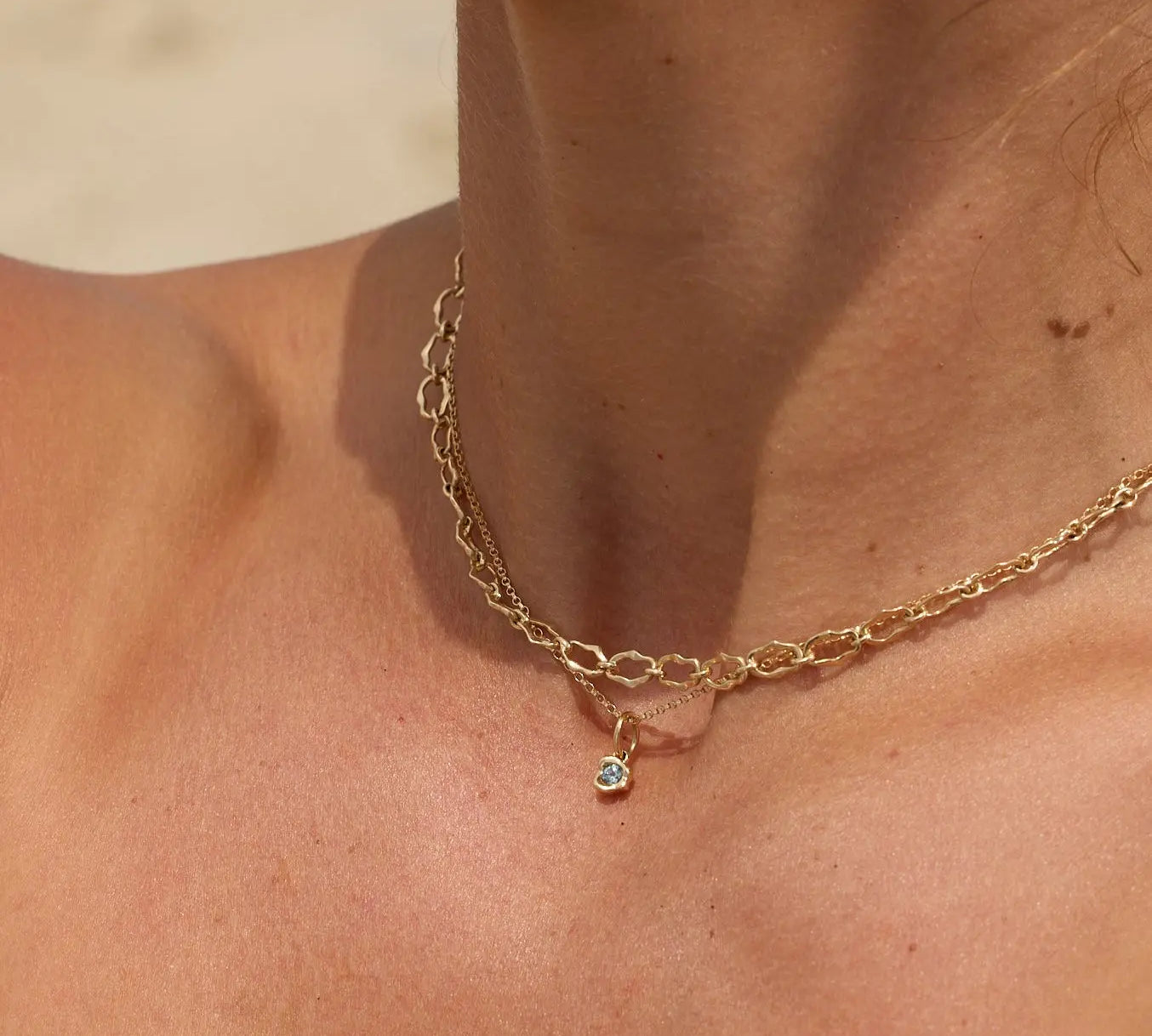 Gold necklace with a small pendant on a person's neck against a neutral background