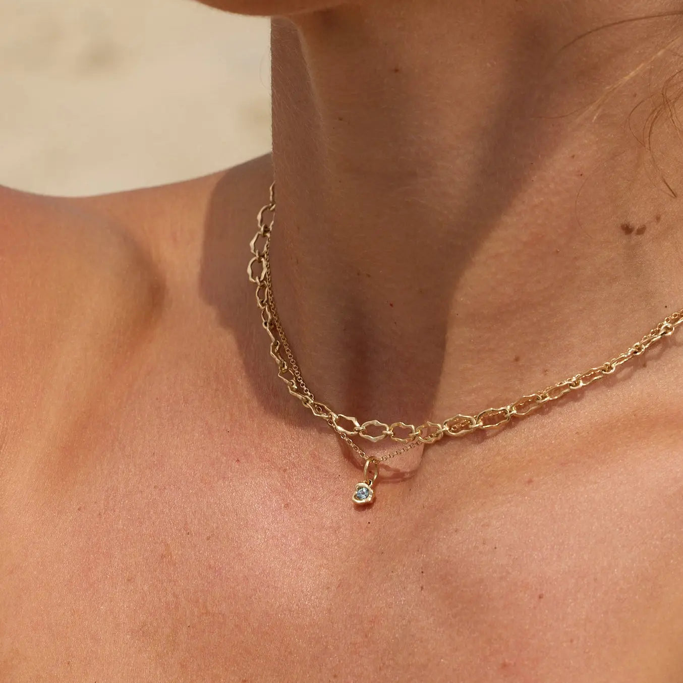Gold necklace with a small pendant on a person's neck against a neutral background
