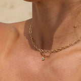 Gold necklace with a small pendant on a person's neck against a neutral background
