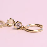 Gold hoop earrings with a diamond on a pink background