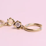 Gold hoop earrings with a diamond on a pink background