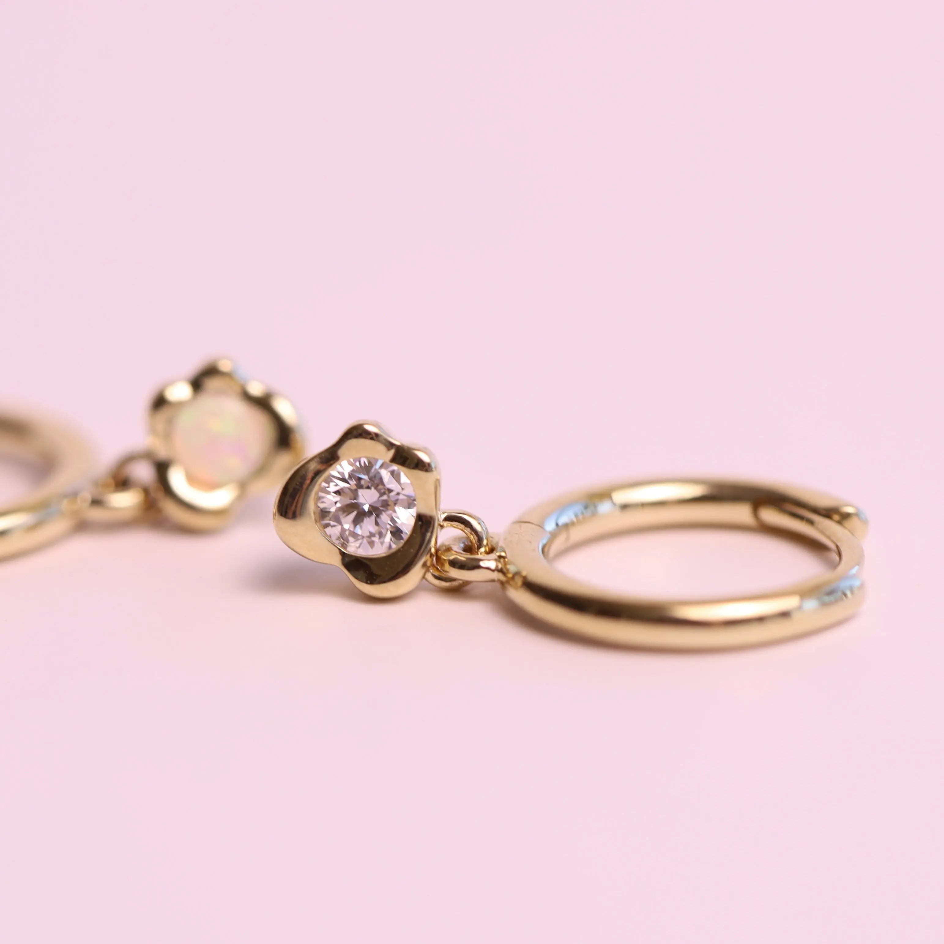 Gold hoop earrings with a diamond on a pink background