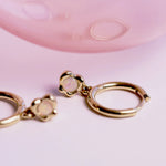 Gold hoop earrings with a opal gemstone on a pink background