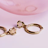 Gold hoop earrings with a opal gemstone on a pink background