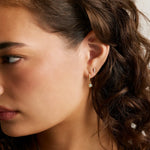 close up of woman's side profile with brown curly hair wearing opal drop hoops and a 3 diamond stud on second piercing.