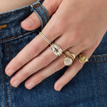 Hand wearing multiple gold rings on a denim background