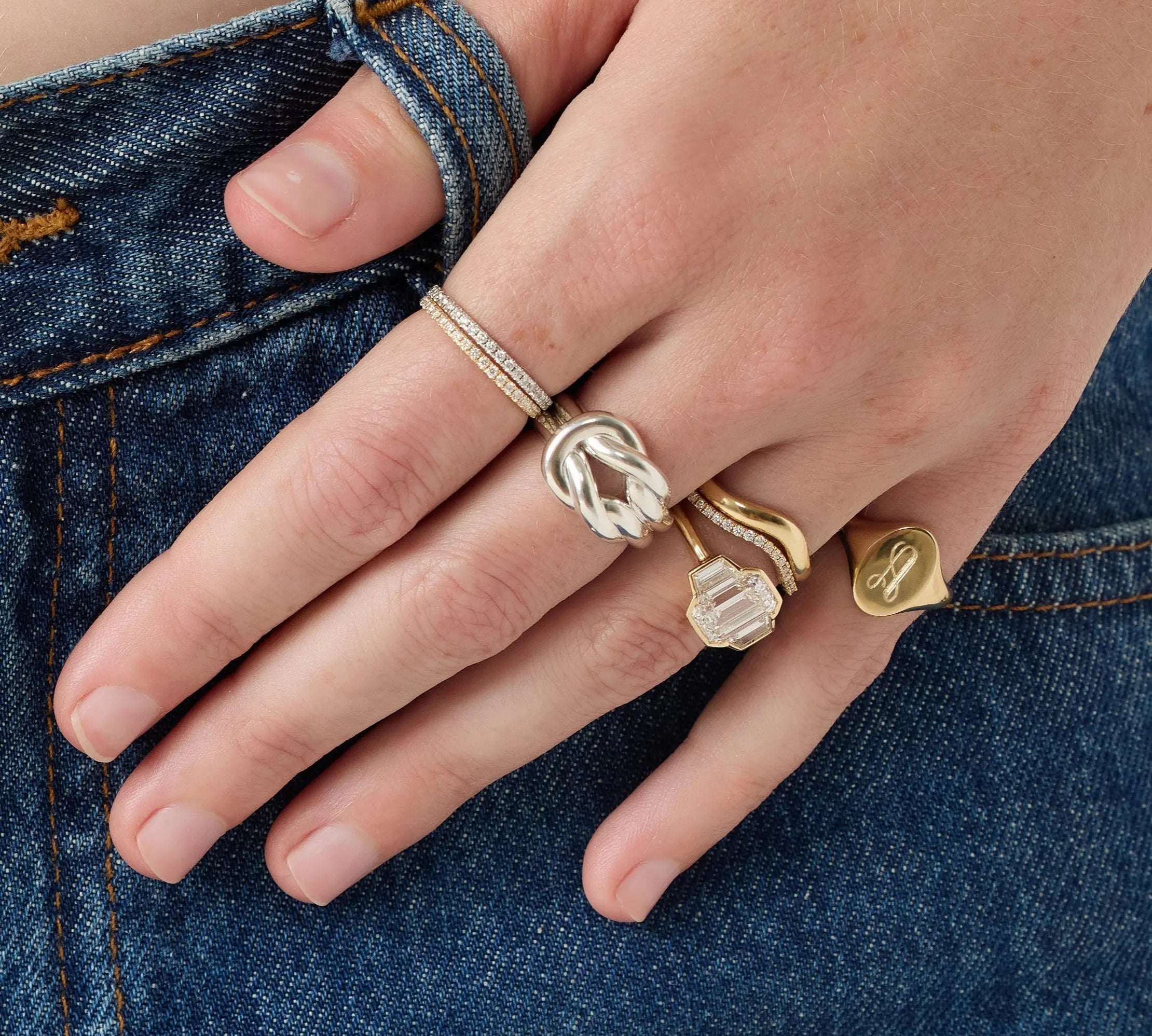 Hand wearing multiple gold rings on a denim background
