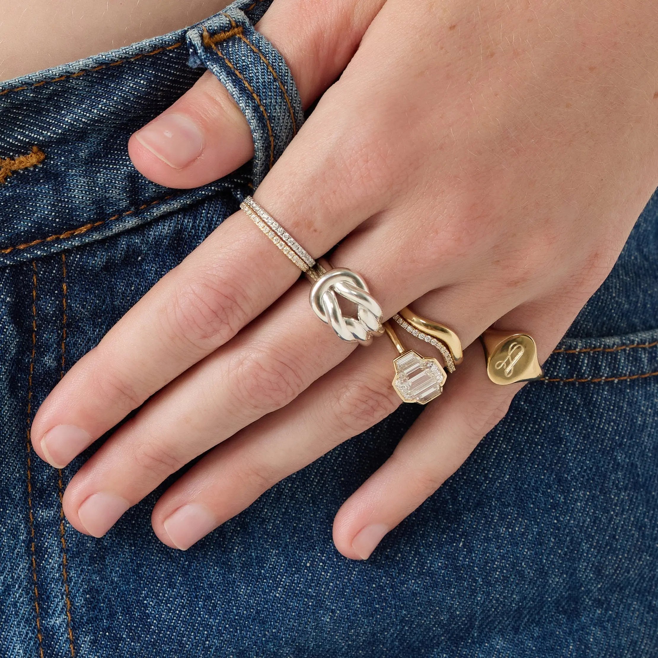 Hand wearing multiple gold rings on a denim background