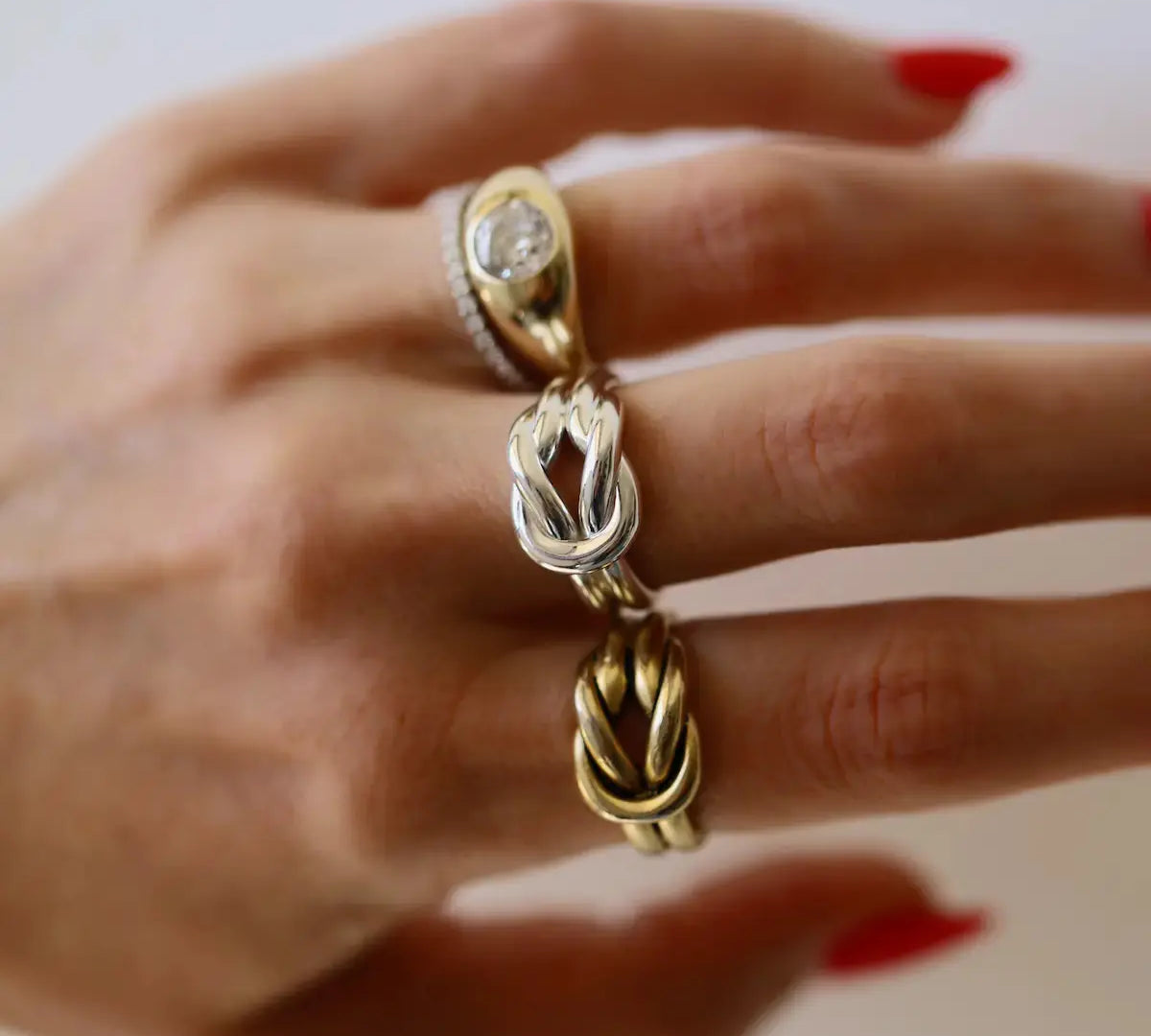 Hand wearing three rings with intricate designs on a neutral background
