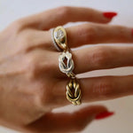 Hand wearing three rings with intricate designs on a neutral background