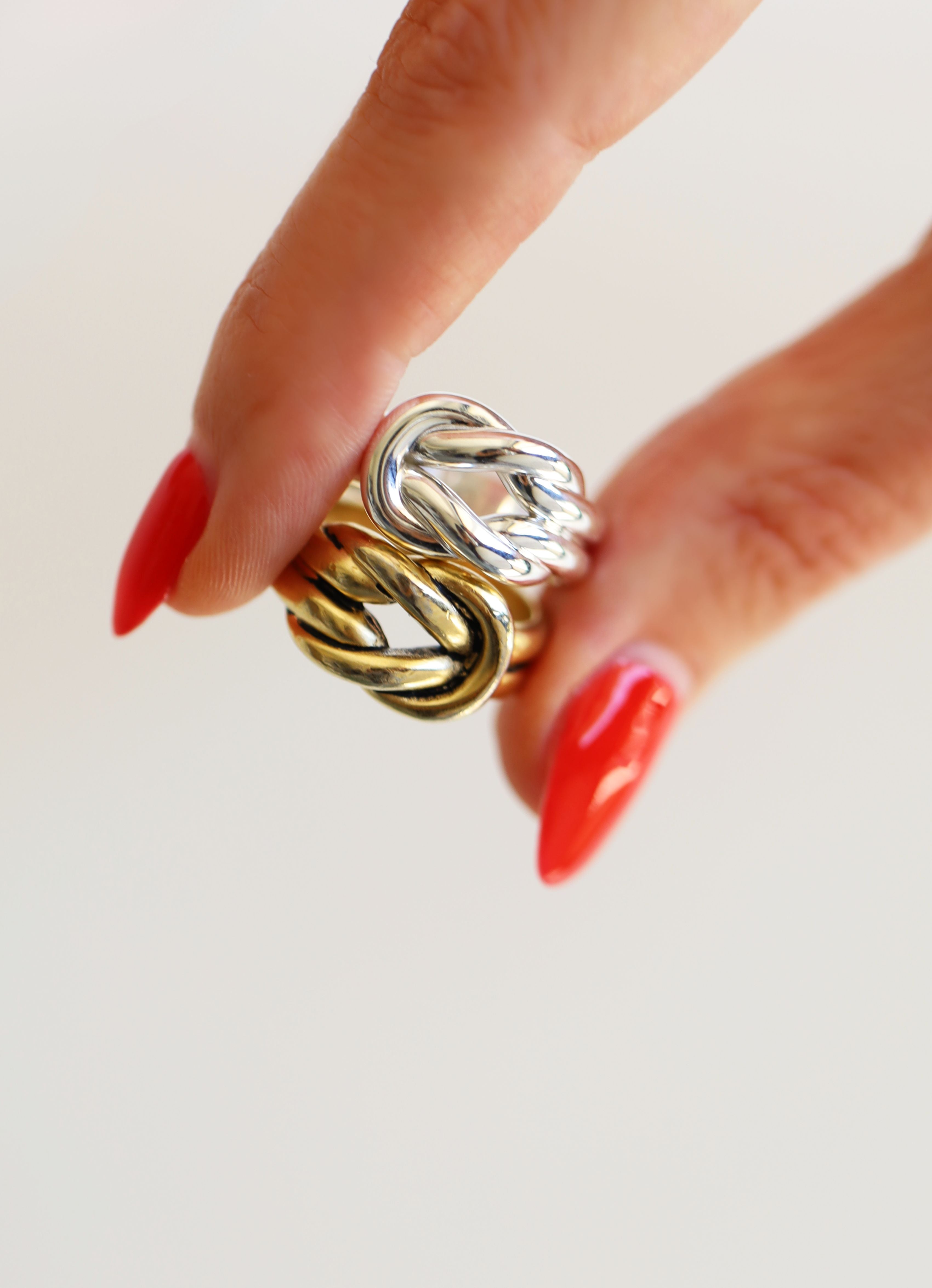 Gold and silver knotted ring on a hand with red nail polish against a light background