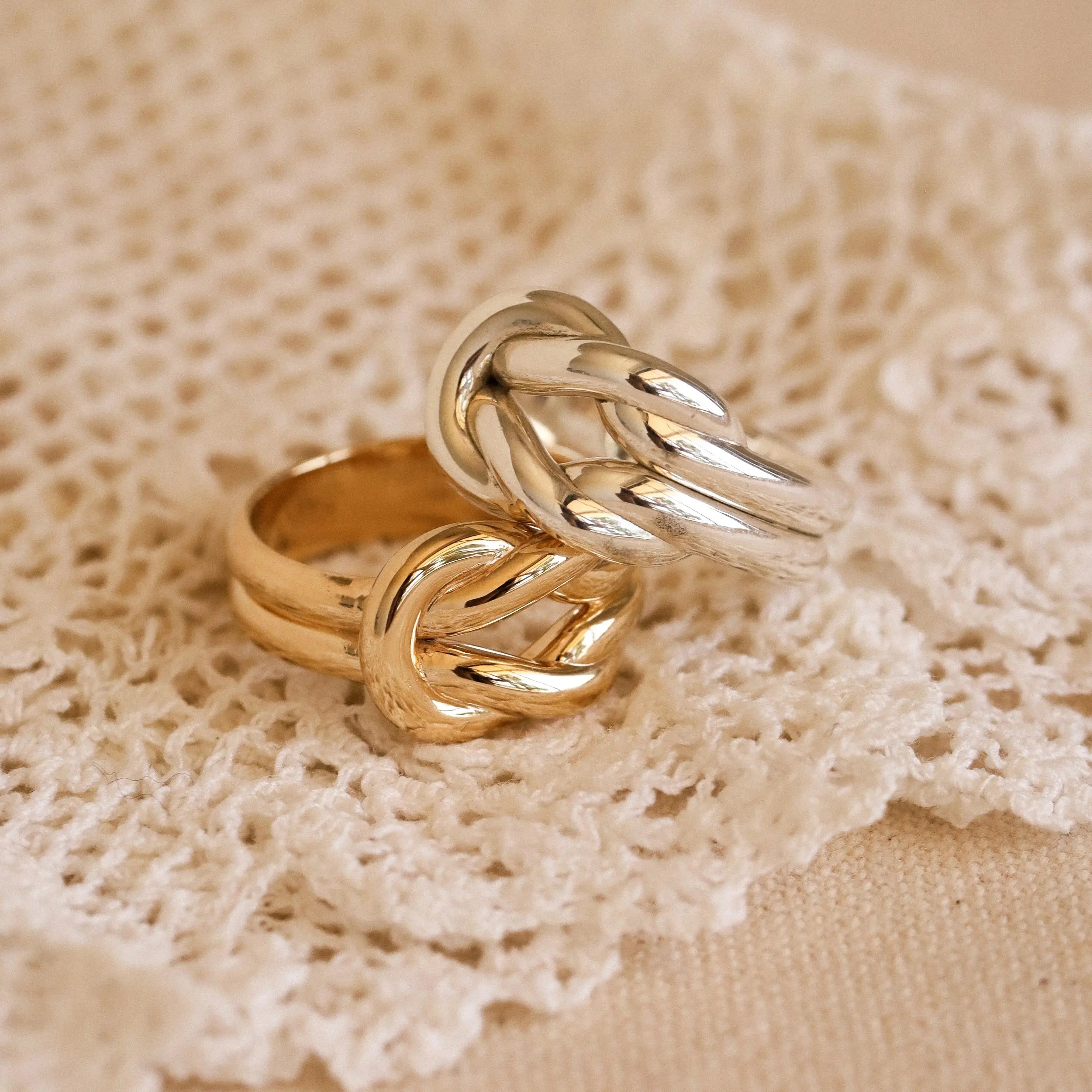 Two gold and silver knotted rings on a lace fabric background
