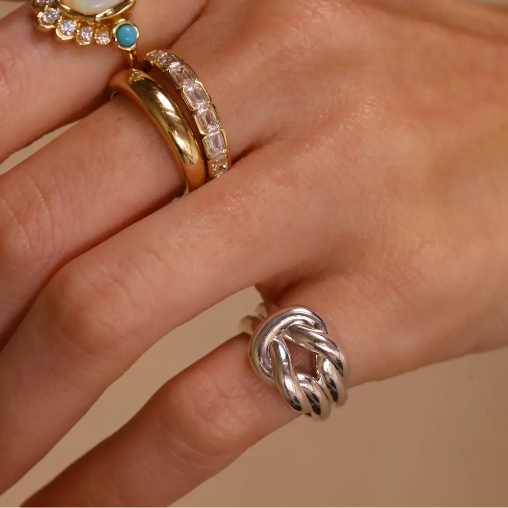 Hand wearing multiple rings with gemstones on a beige background