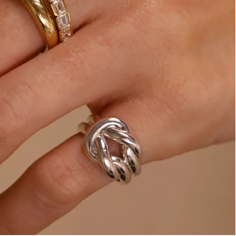 Hand wearing multiple rings with gemstones on a beige background