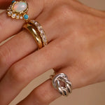 Hand wearing multiple rings with gemstones on a beige background