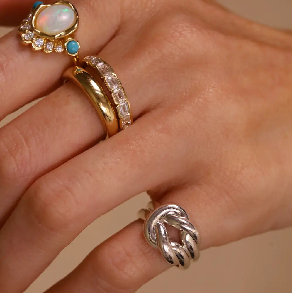 Hand wearing multiple rings with gemstones on a beige background