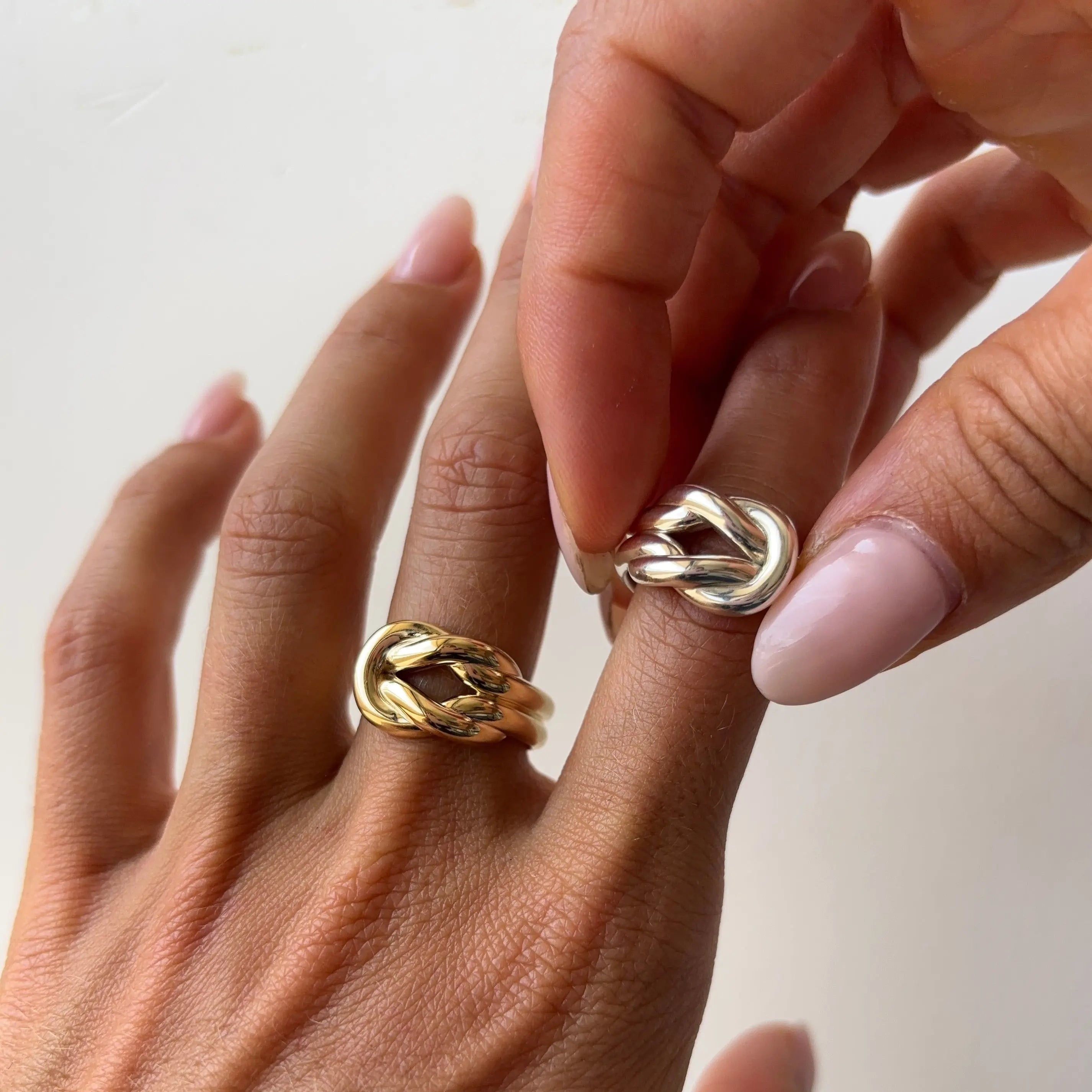 Close-up of hands wearing gold and silver knot on a neutral background