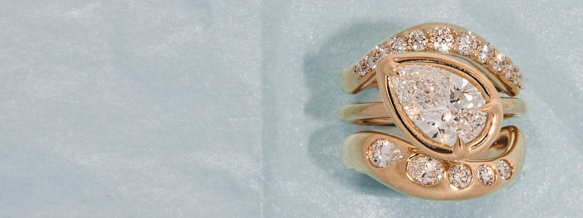 A close-up of a gold ring with a marquise-shaped clear gemstone and smaller surrounding stones, photographed on a pale blue textured background.