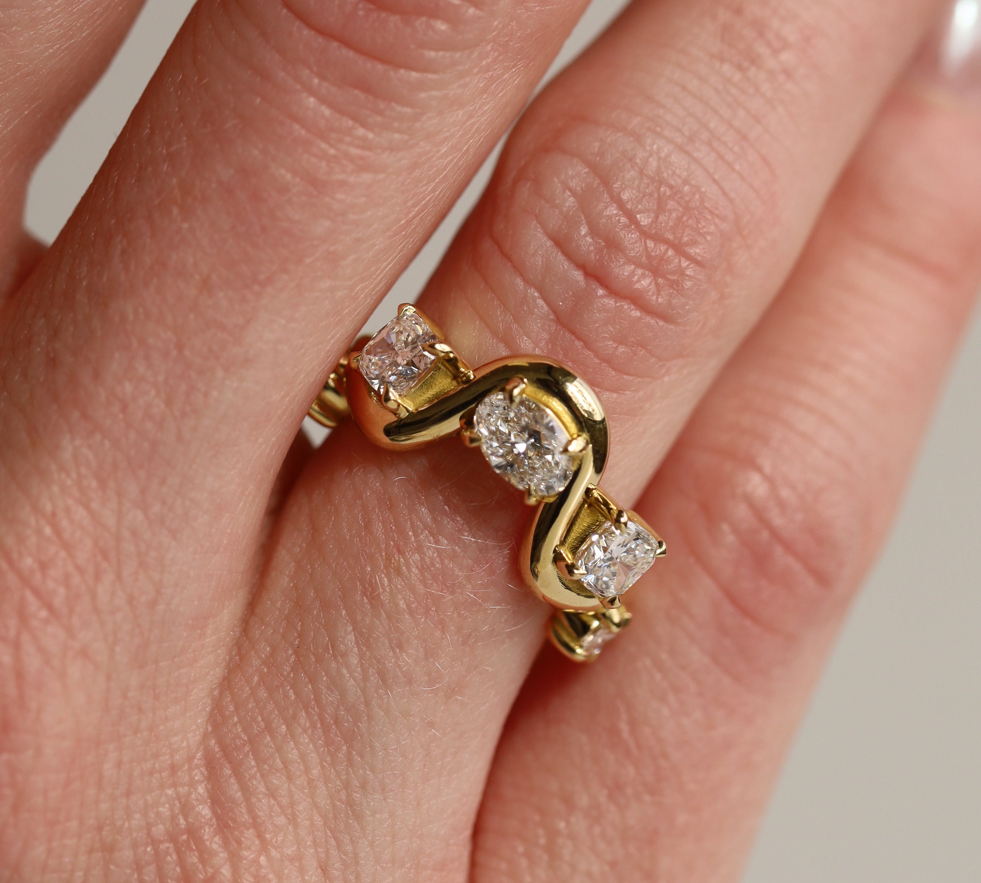 Gold ring with diamonds on a finger against a neutral background