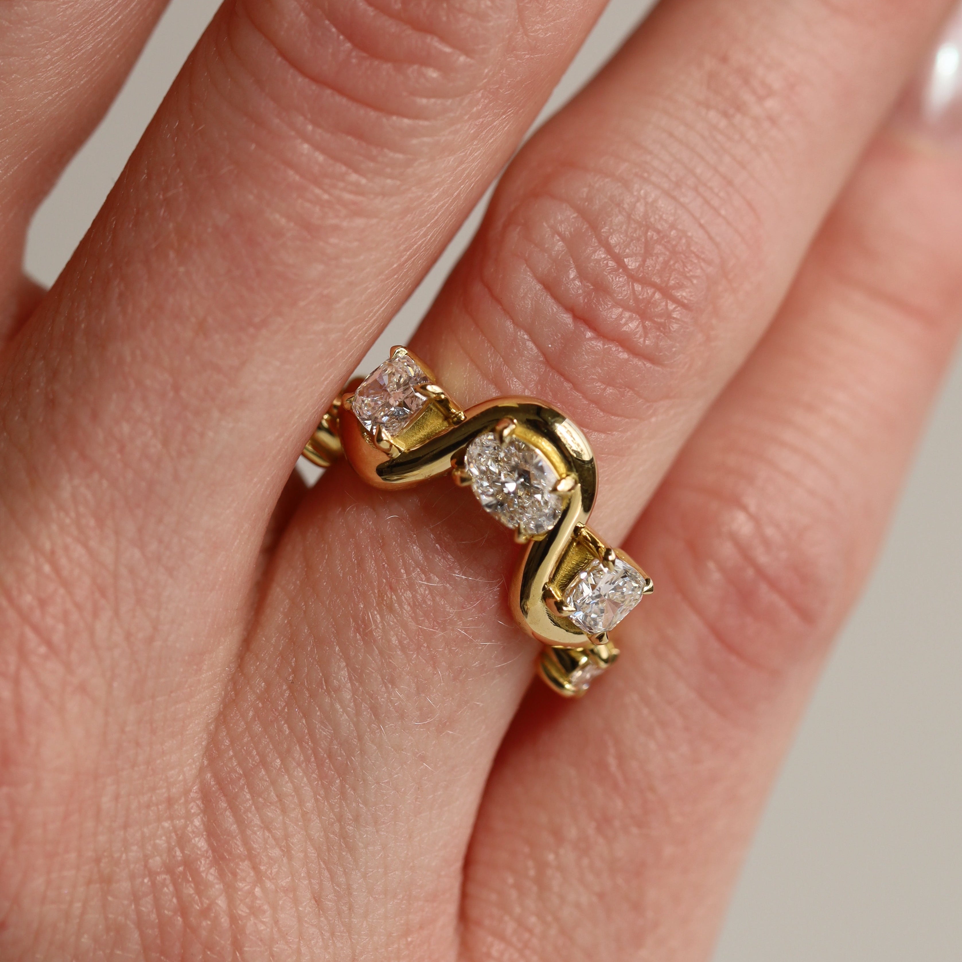 Gold ring with diamonds on a finger against a neutral background