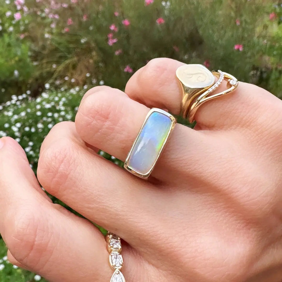 Hand wearing multiple gold rings with gemstones against a blurred natural background