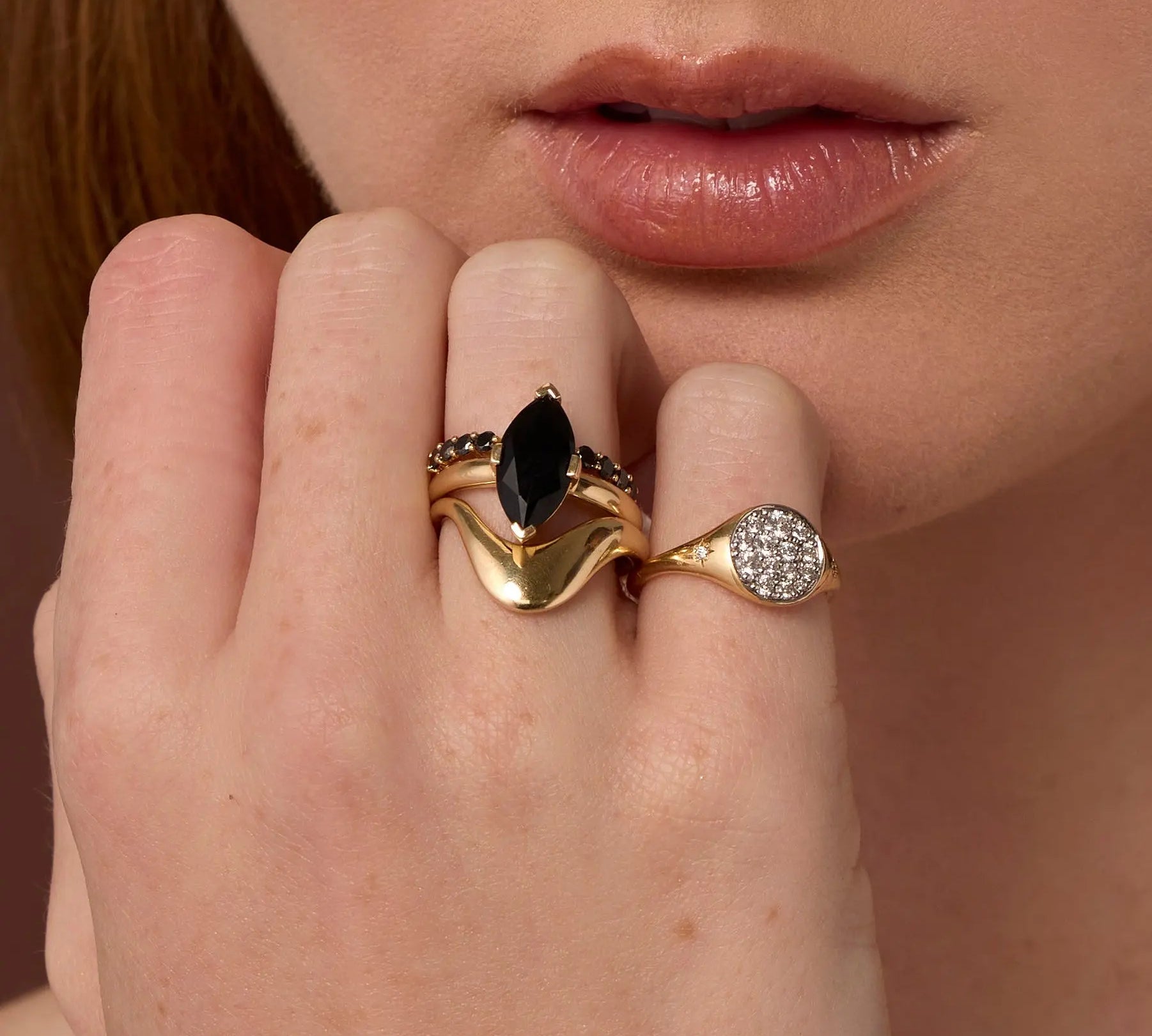 Close up of woman resting hand against her chin, highlighting multiple Marrow Fine rings styled and stacked together