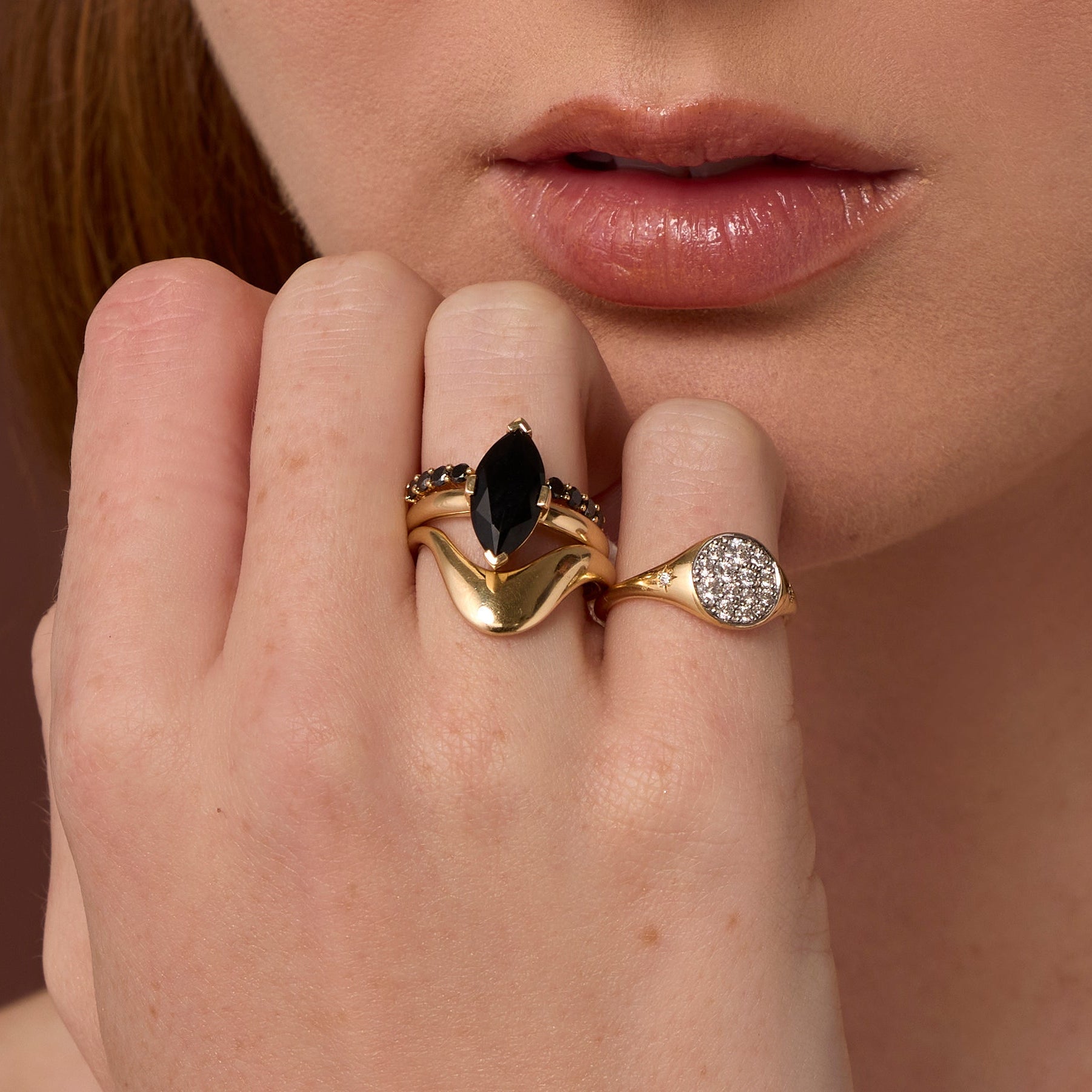 Close up of woman resting hand against her chin, highlighting multiple Marrow Fine rings styled and stacked together