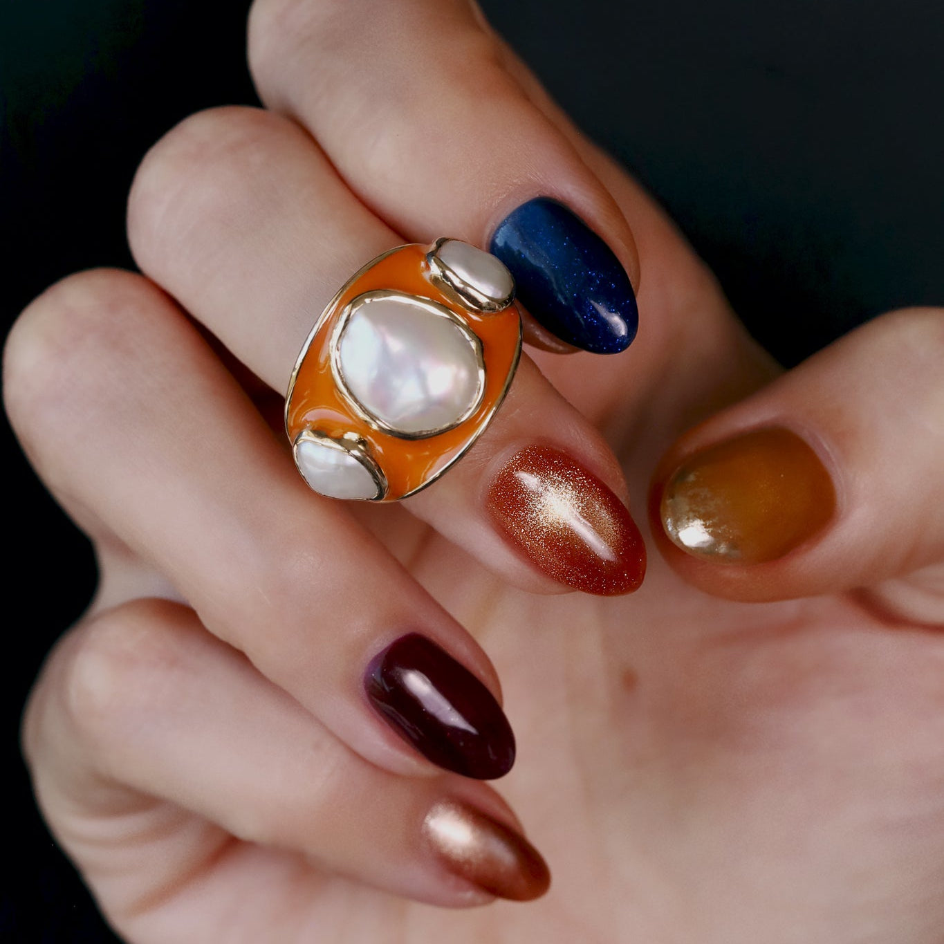Baroque Keshi Pearl and Burnt Orange Enamel Ring worn on the hand against a dark background