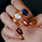 Baroque Keshi Pearl and Burnt Orange Enamel Ring worn on the hand against a dark background