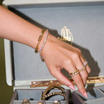 Hand wearing gold and pink jewelry with a jewelry box in the background