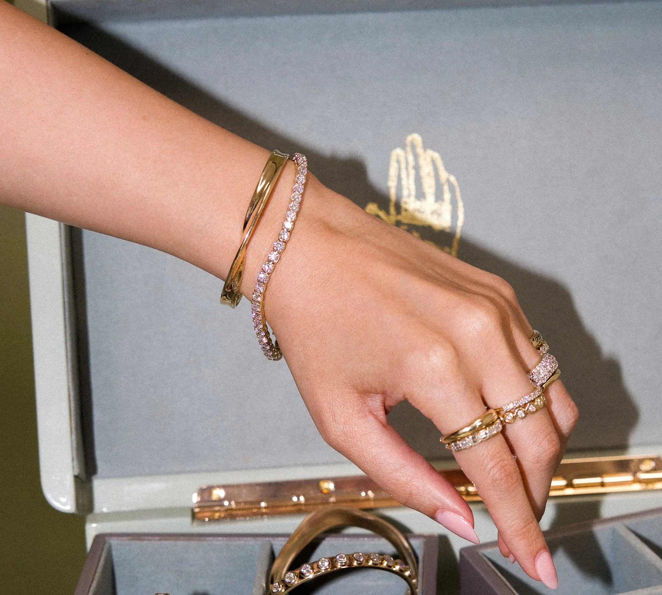 Hand wearing gold and pink jewelry with a jewelry box in the background