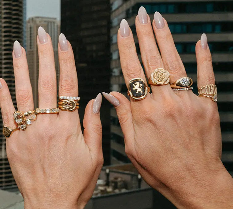 Two hands wearing multiple gold rings with a cityscape background
