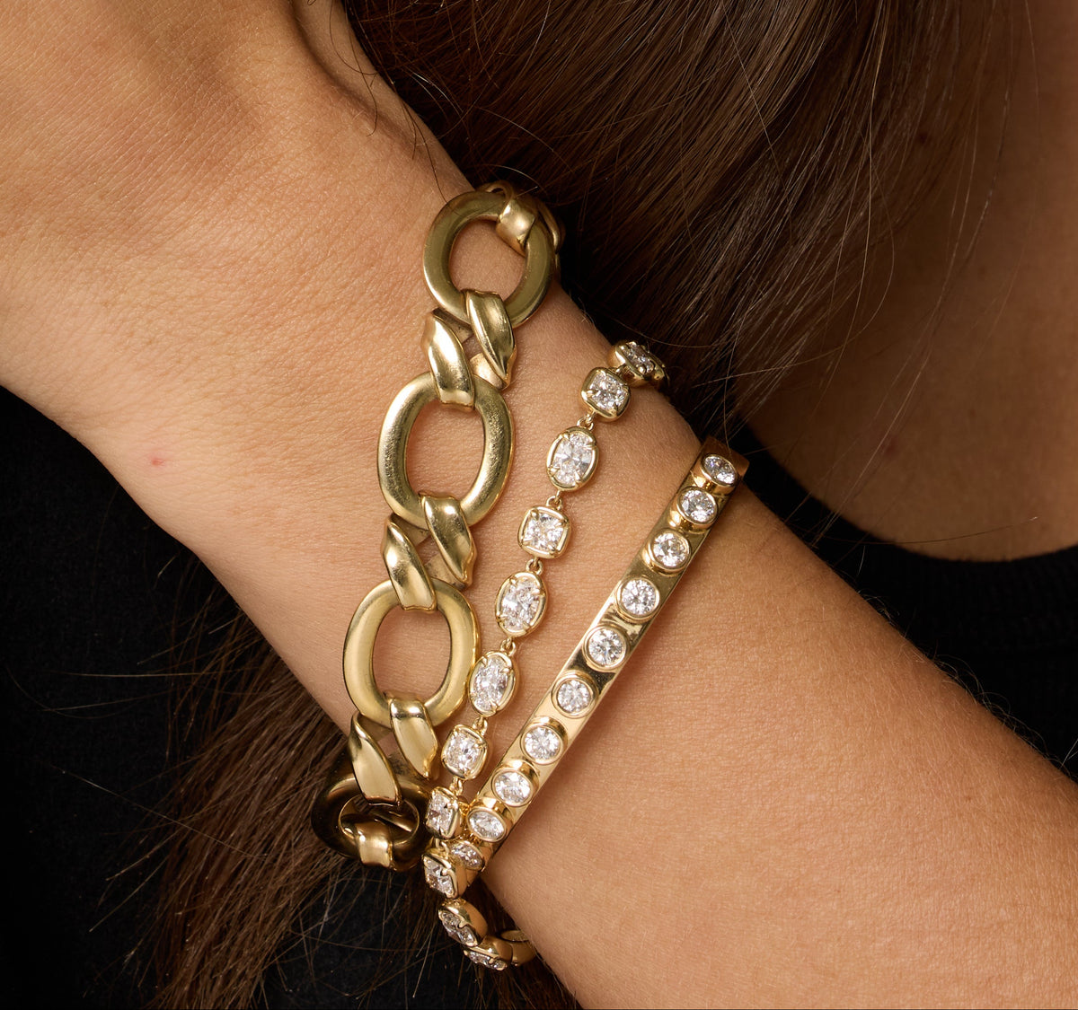 Wrist stacked with a chunky gold chain bracelet and diamond tennis bracelets