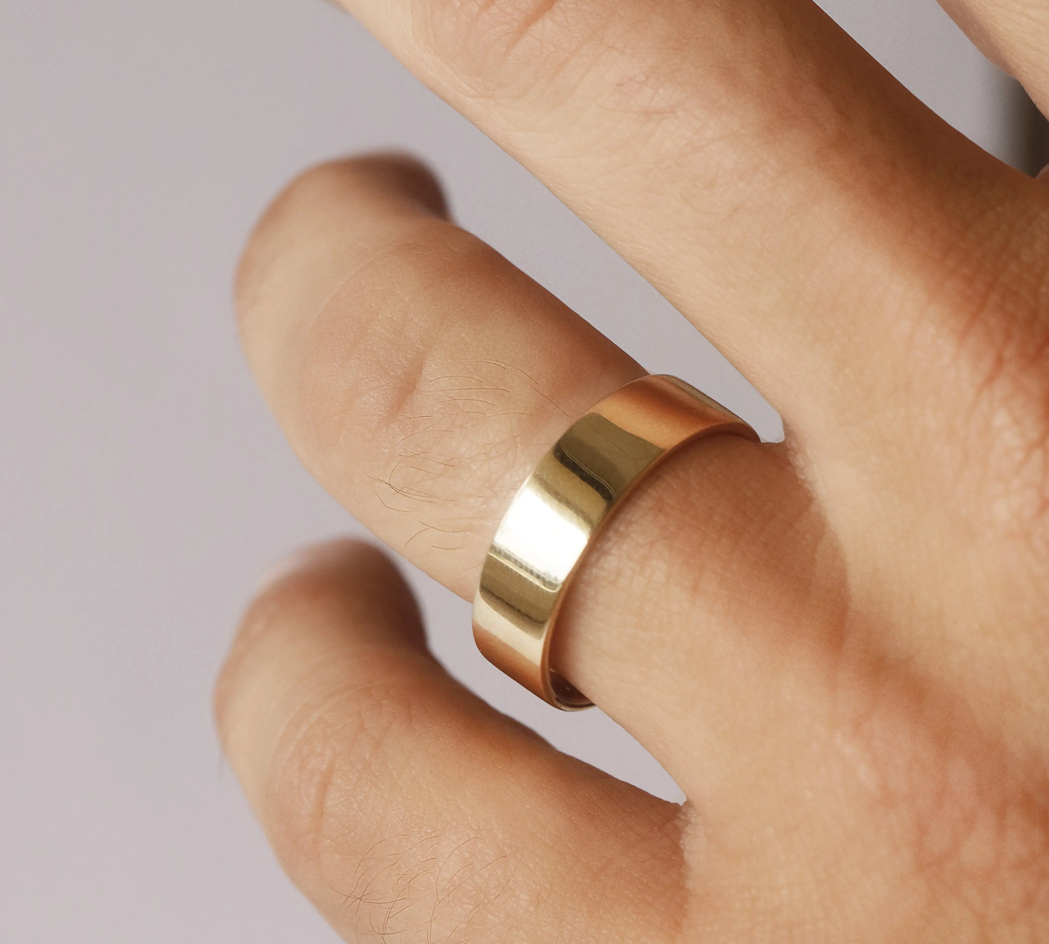 Gold ring on a finger against a neutral background