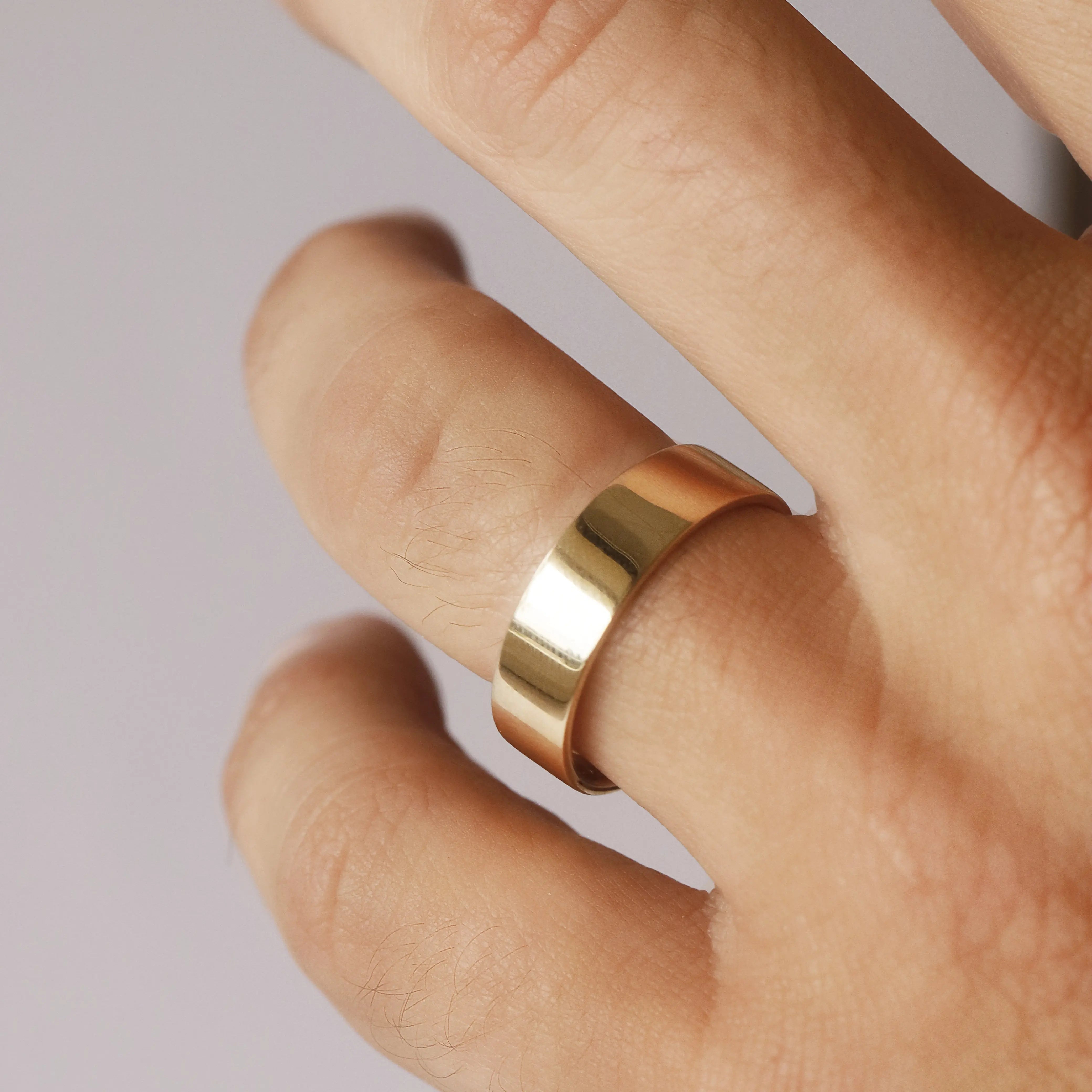 Gold ring on a finger against a neutral background