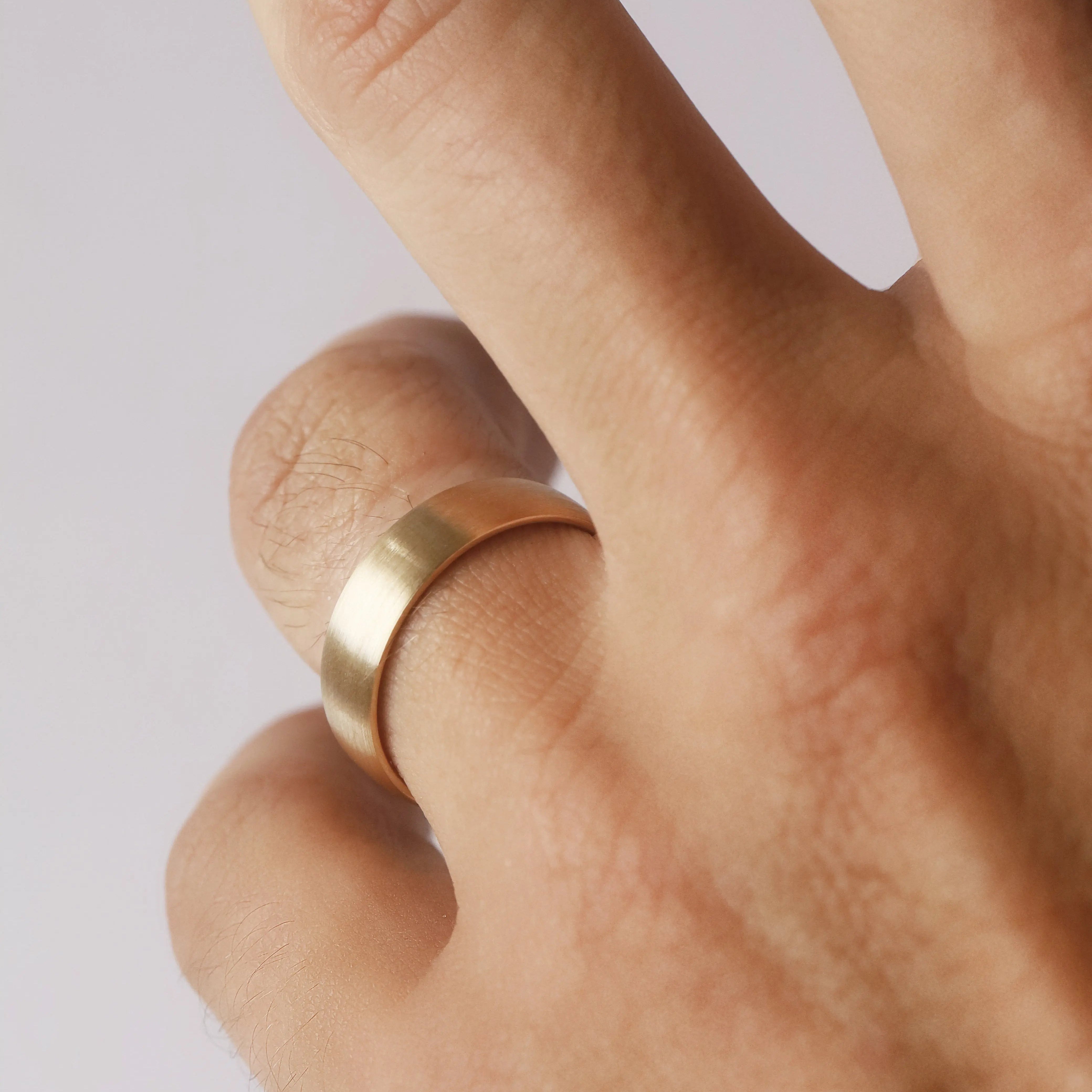 Gold ring on a finger against a light background