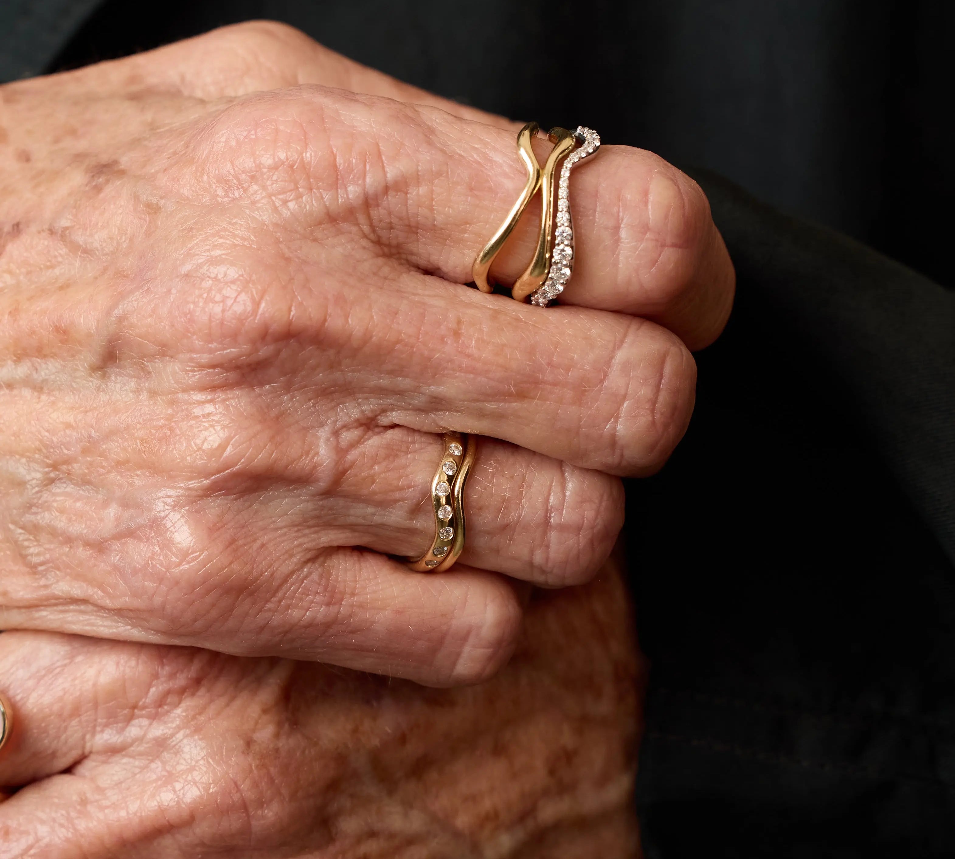 Close-up of an elderly hand wearing two gold rings with a dark background