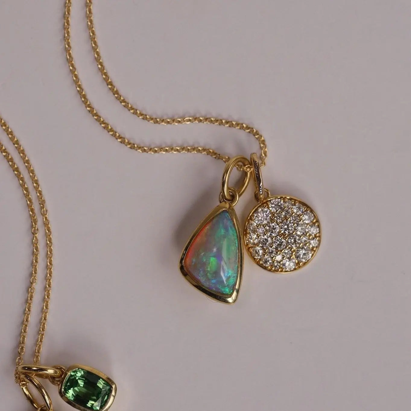 Gold necklace with opal and diamond pendants on a light gray background
