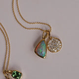Gold necklace with opal and diamond pendants on a light gray background