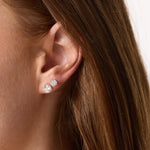 Close-up of a person wearing two diamond stud earrings with a neutral background.