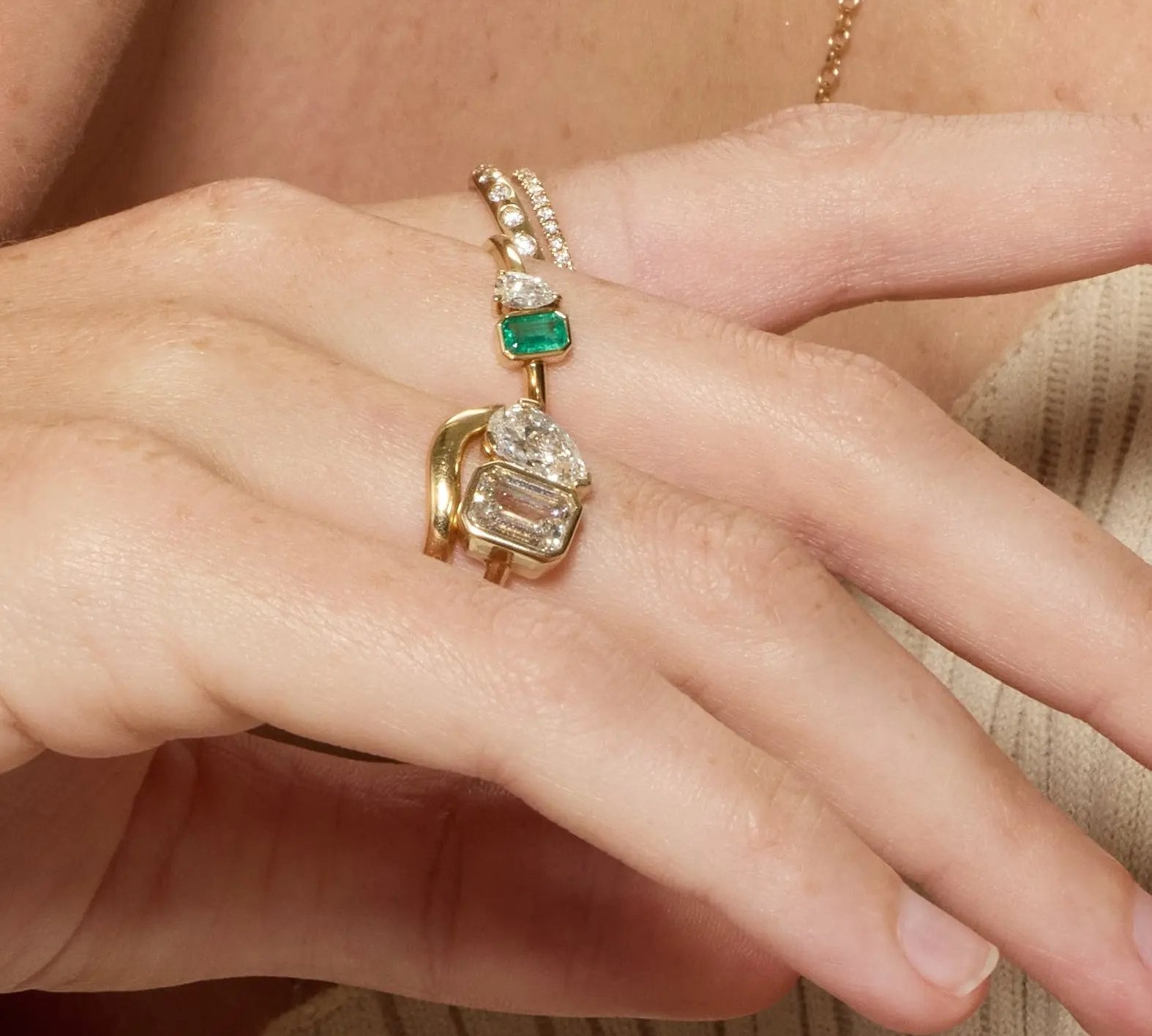 Close-up of a hand wearing two gold rings with gemstones on a neutral background