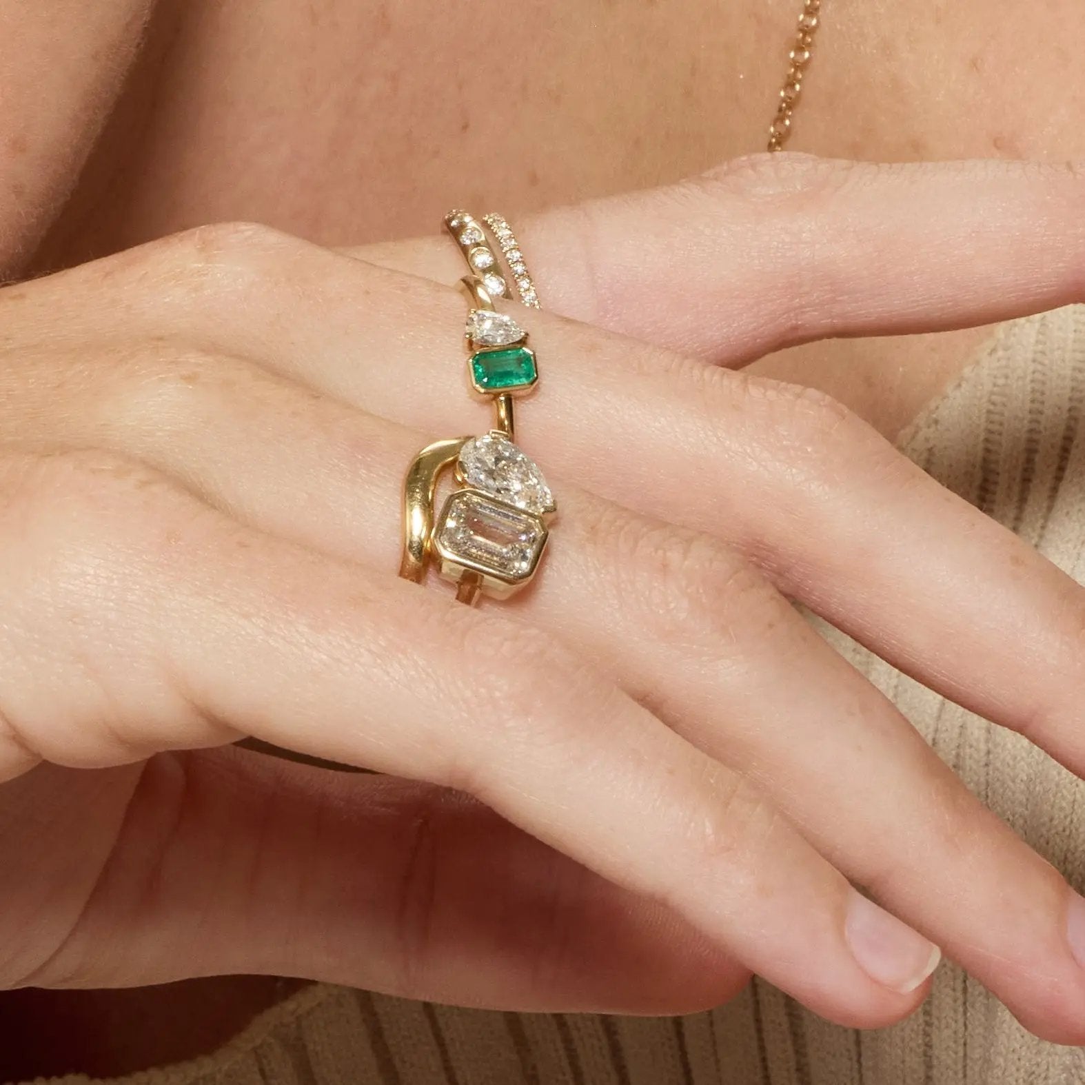 Close-up of a hand wearing two gold rings with gemstones on a neutral background