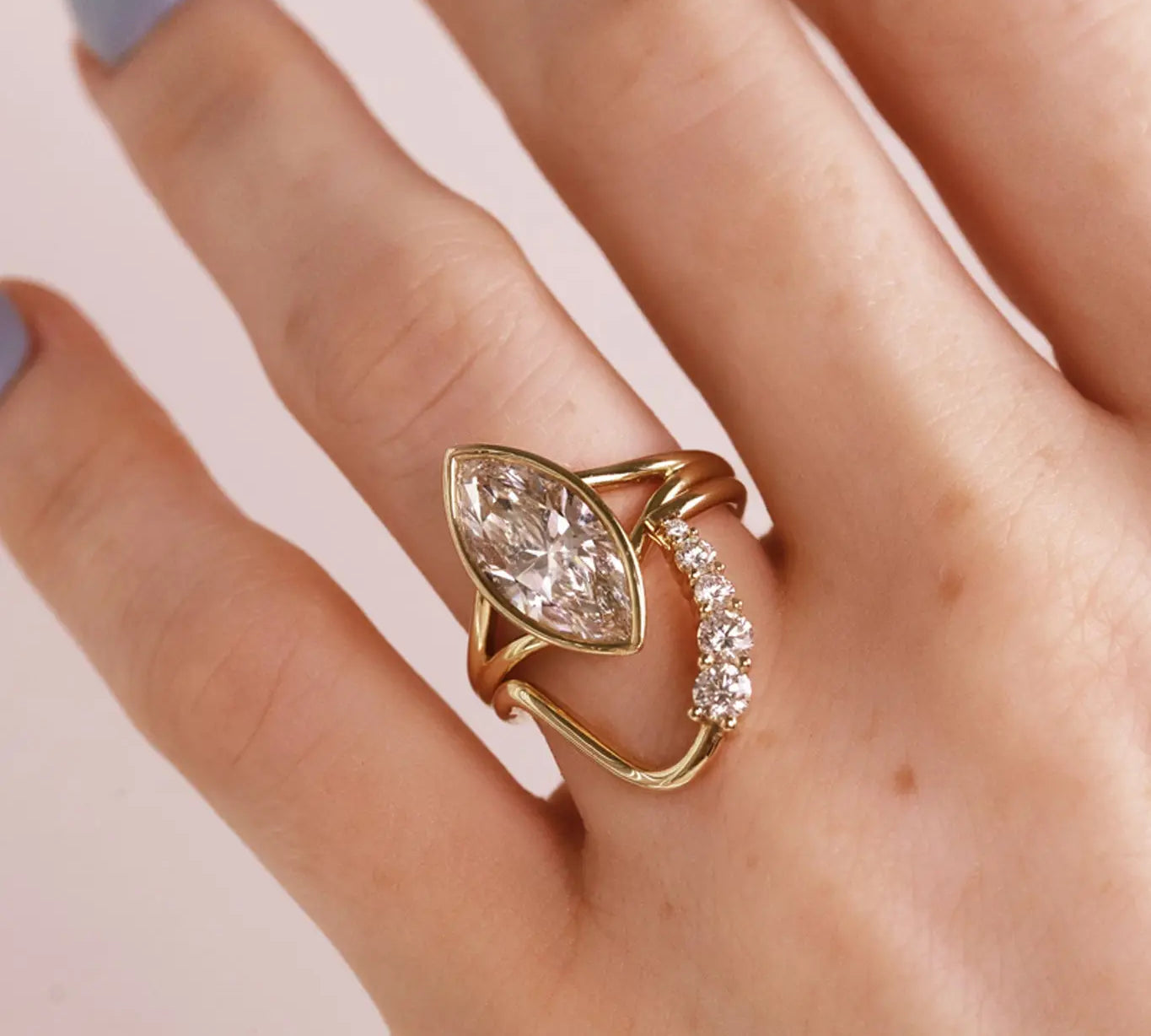 A gold ring with a marquise-cut clear diamond on split shank. Stacked with a wavy diamond band. Shown worn on a hand.