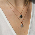 Two gold necklaces with pendants on a person wearing a white top.