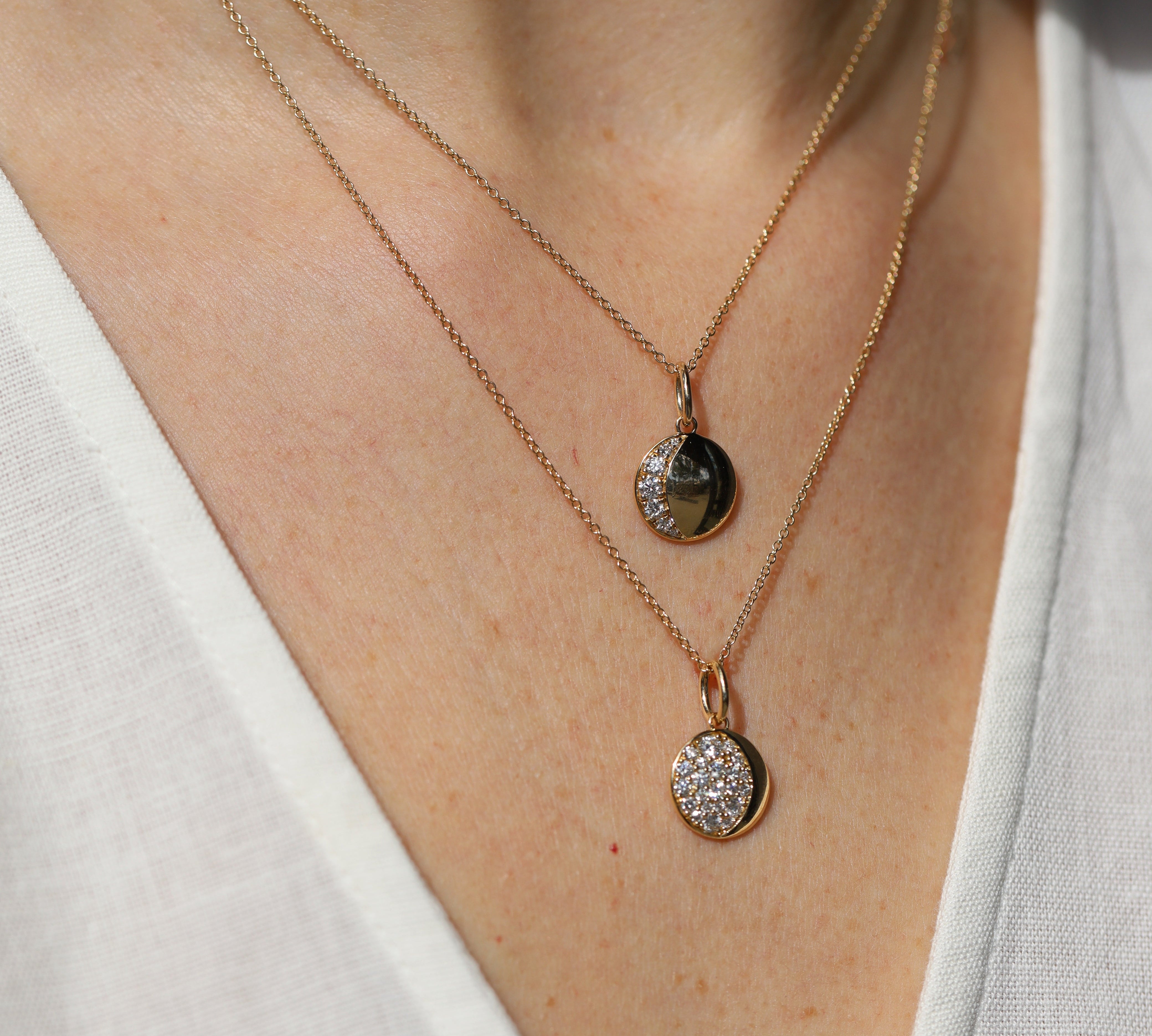 Two gold necklaces with pendants on a person wearing a white top.