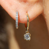 Gold hoop earrings with diamond accents worn on an ear against a blurred background