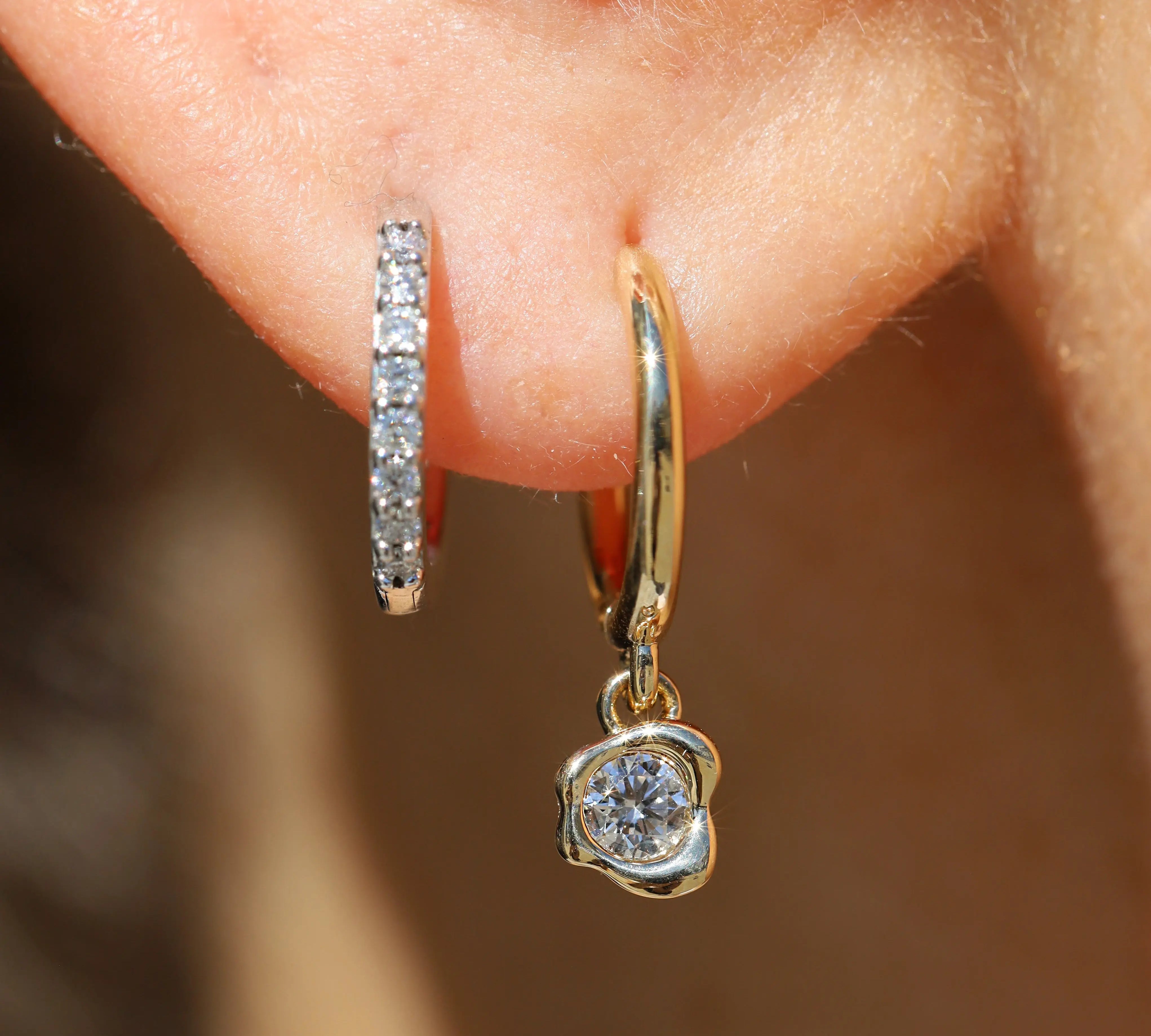Gold hoop earrings with diamond accents worn on an ear against a blurred background