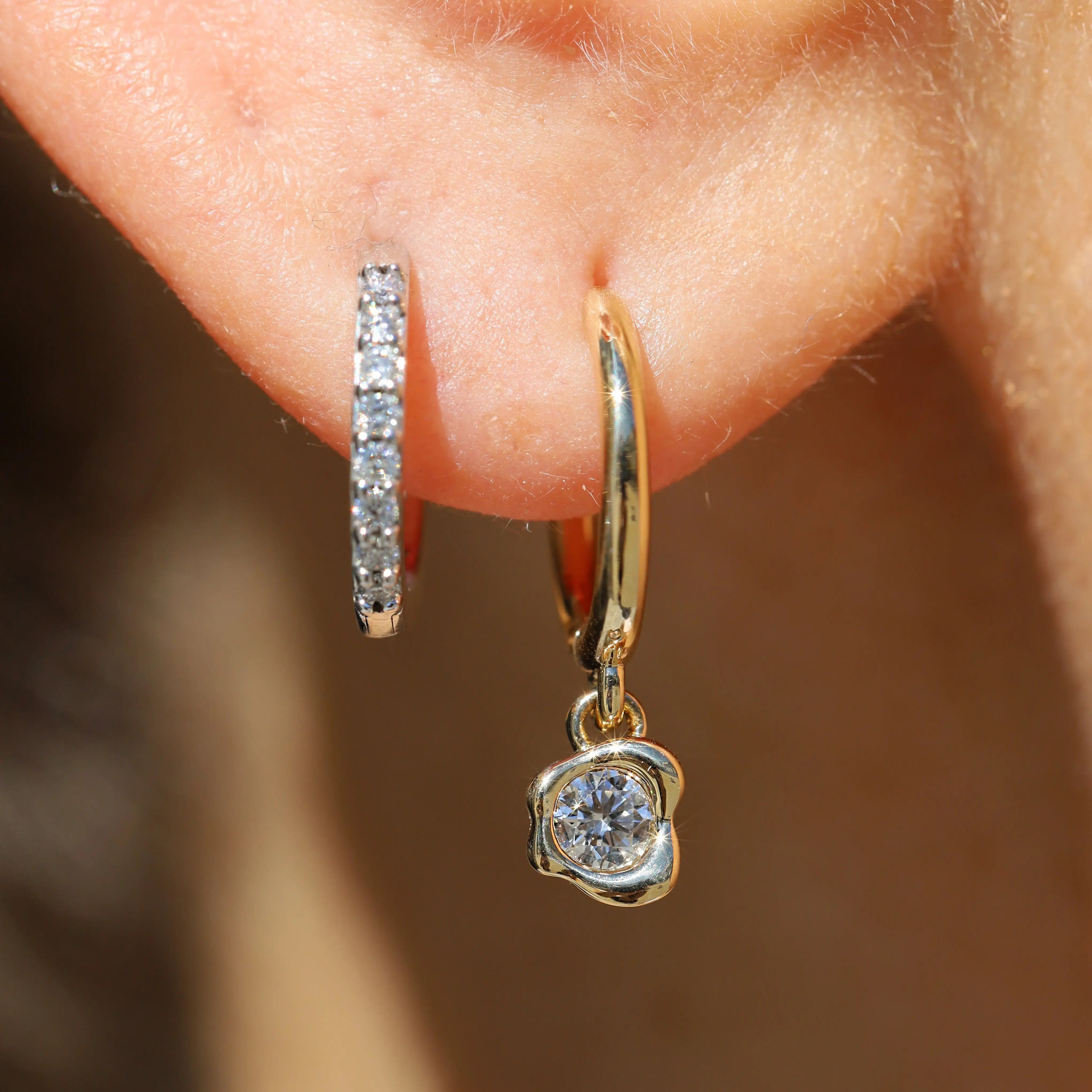 Gold hoop earrings with diamond accents worn on an ear against a blurred background