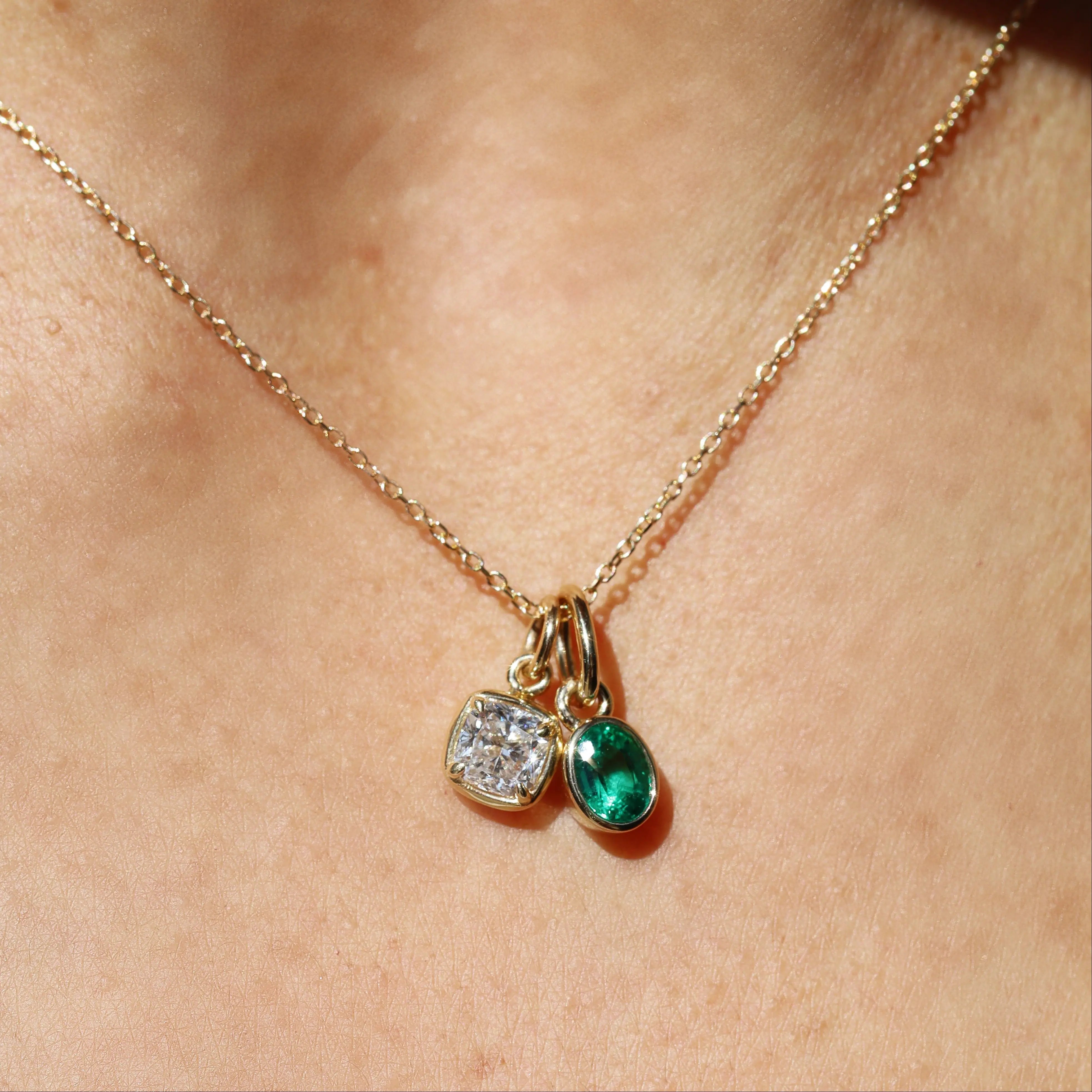 Necklace with two charms, one green and one clear, on a person's neck.