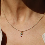 Necklace with a pendant featuring a green gemstone and small white gemstone on a person's neck.
